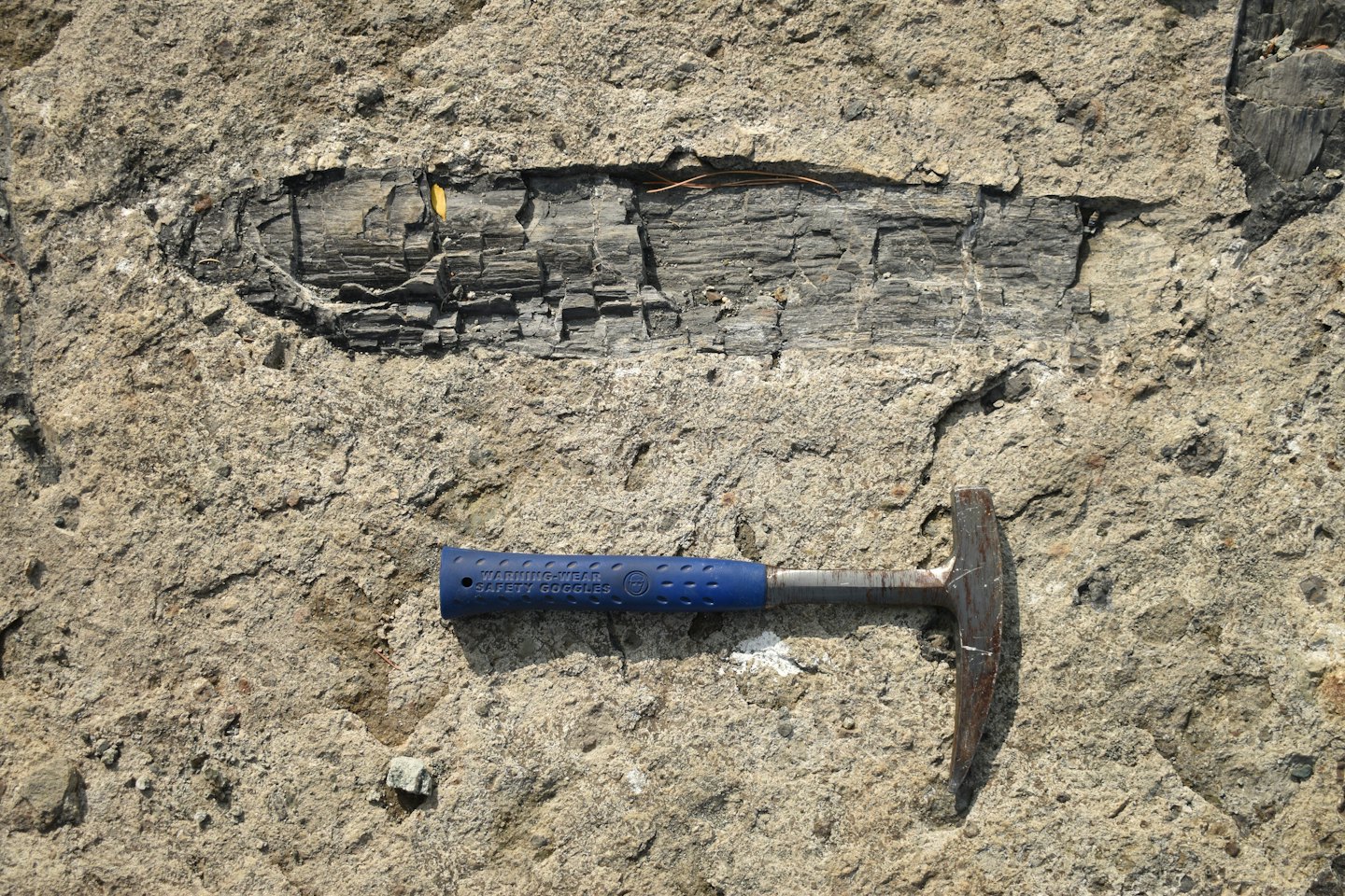 Un martello da roccia in metallo appoggiato su una formazione geologica texturizzata.