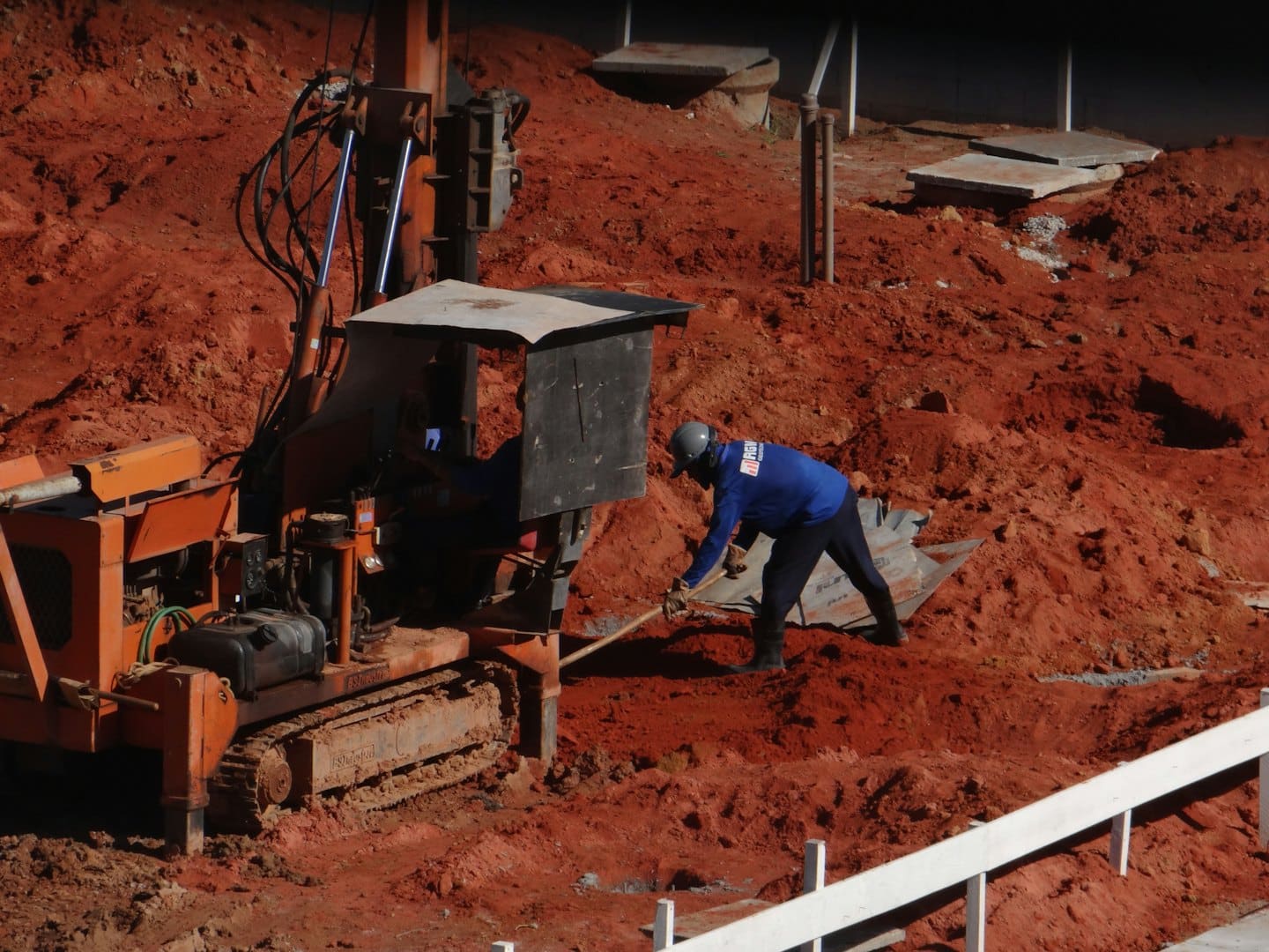 Due operai edili maneggiano macchinari e scavano terra in un cantiere.